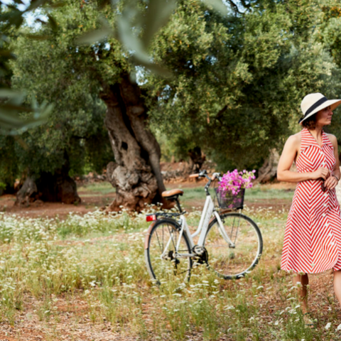 Woman in a red dress with a bicycle in an olive grove.