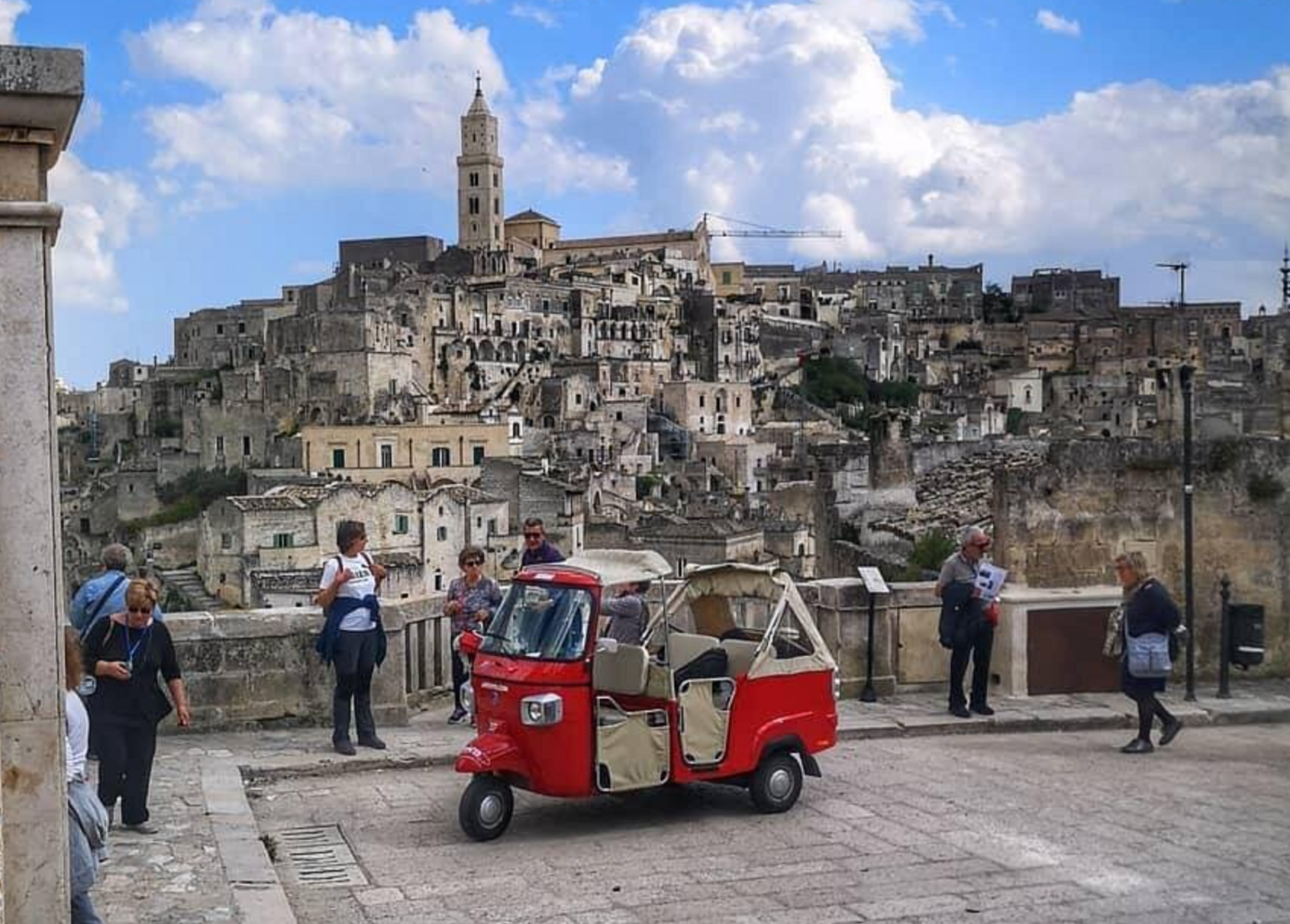 Red tuk-tuk in front of historic stone buildings Matera