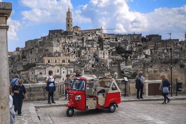 Red tuk-tuk in front of historic stone buildings Matera